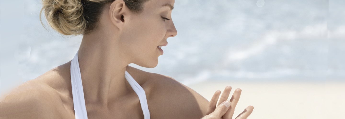 Frau am Strand, die in der Sonne sitzt und ihre Haut mit einem kritischen Blick betrachtet.
