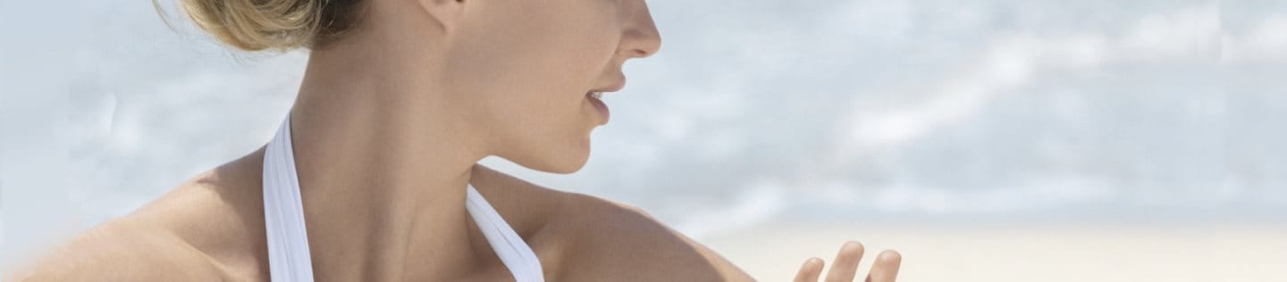 Frau am Strand, die in der Sonne sitzt und ihre Haut mit einem kritischen Blick betrachtet.