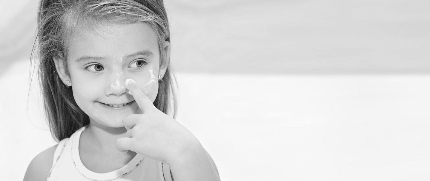 Primer plano de una niña aplicándose crema hidratante en la nariz