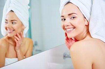 A woman smiling in front of her bathroom mirror wearing a towel