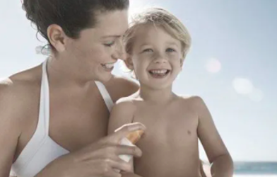 Woman at the beach with her young son applying sun screen to him