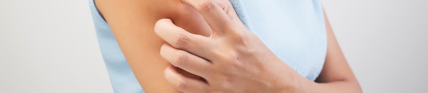 A woman scratches her dry skin on her arm.