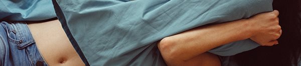 Woman laying in bed covering her face with a pillow