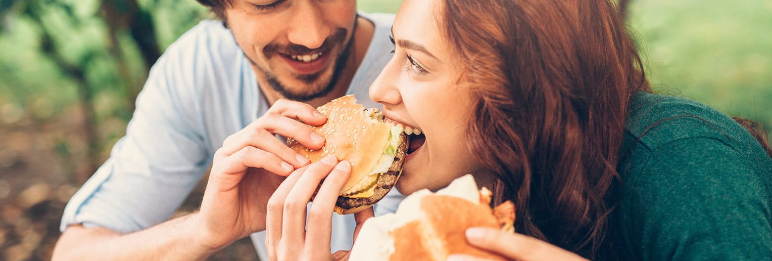 fiatal pár közül a férfi hamburgert kínál a nőnek