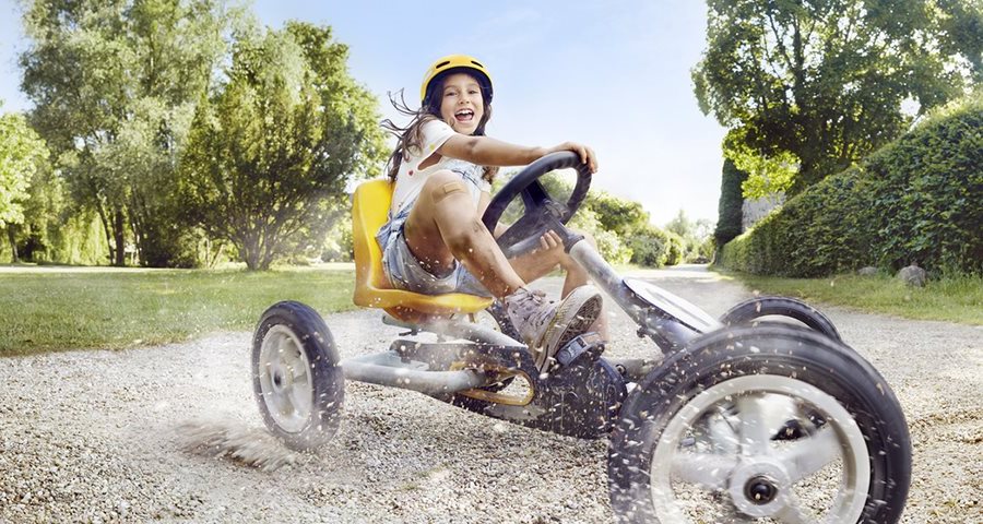 A young girl on a yellow tricycle smiles as she skids across a gravel path