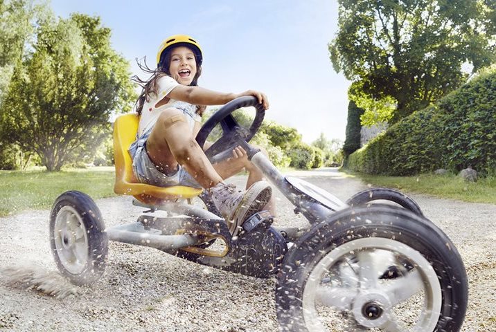A young girl on a yellow tricycle smiles as she skids across a gravel path