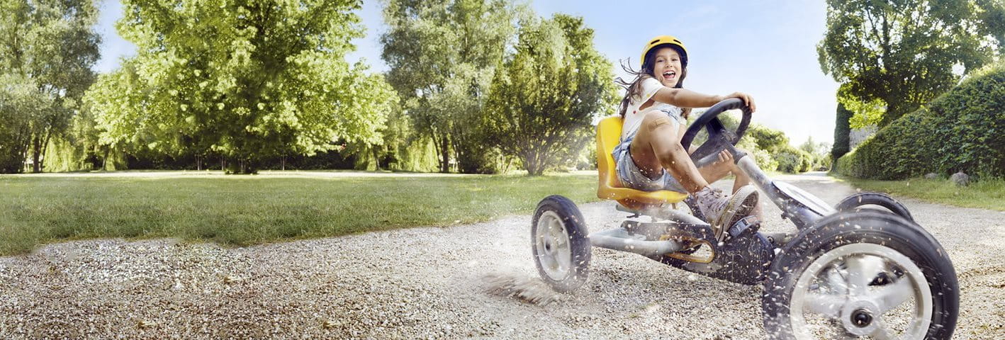 A young girl on a yellow tricycle smiles as she skids across a gravel path