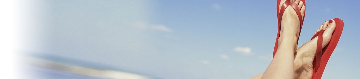 Feet in red flip flops with blue sky in background