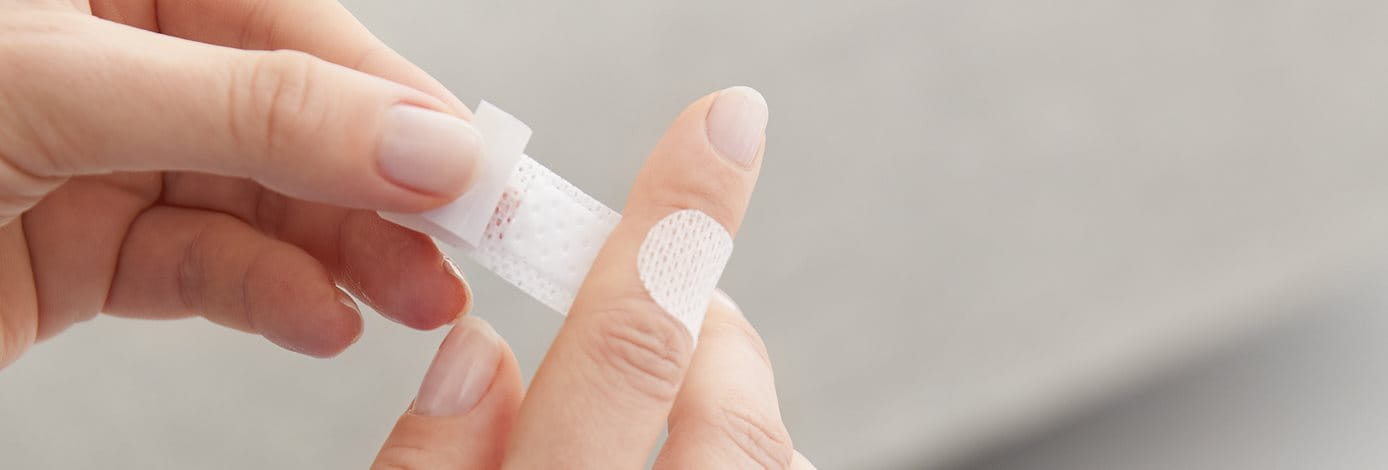 Detailansicht einer Person, die ein Pflaster auf den Zeigefinger klebt.