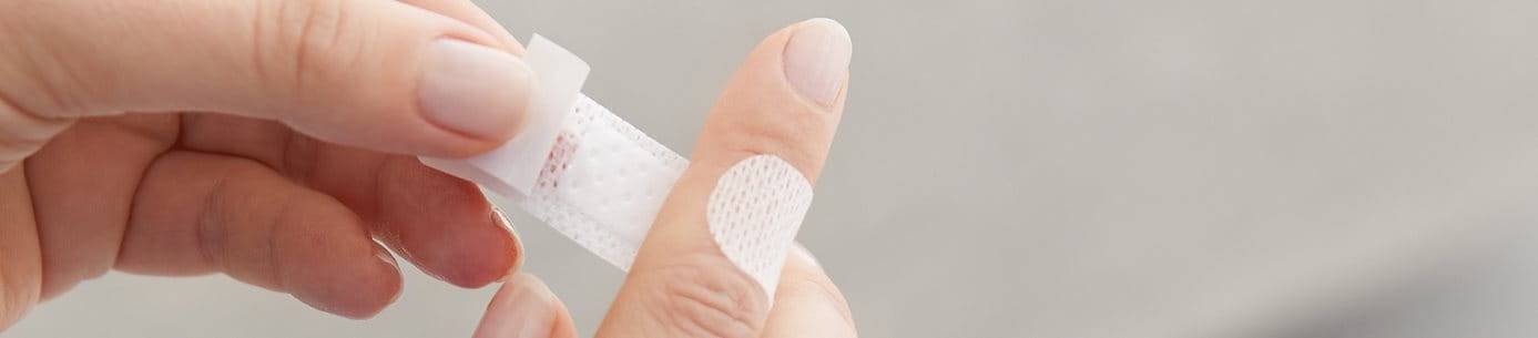 Detailansicht einer Person, die ein Pflaster auf den Zeigefinger klebt.