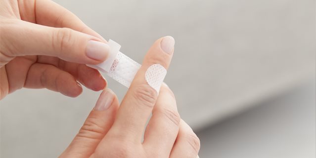 Detailansicht einer Person, die ein Pflaster auf den Zeigefinger klebt.