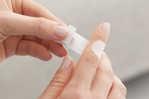 Detailansicht einer Person, die ein Pflaster auf den Zeigefinger klebt.