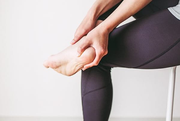 Ein Mann, der schmerzerfüllt seinen Fuß mit Fersensporn betrachtet.