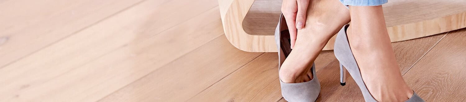 Frau in Pumps greift mit der Hand an die Ferse Ihres Fußes