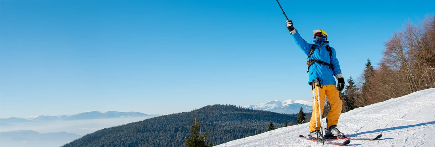 Skifahrer steht auf der schneebedeckten Piste und zeigt mit Skistock in die Luft