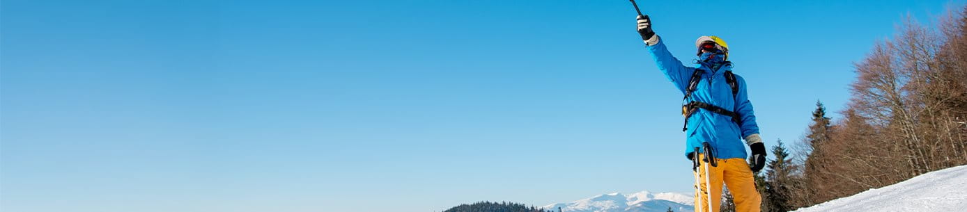 Skifahrer steht auf der schneebedeckten Piste und zeigt mit Skistock in die Luft