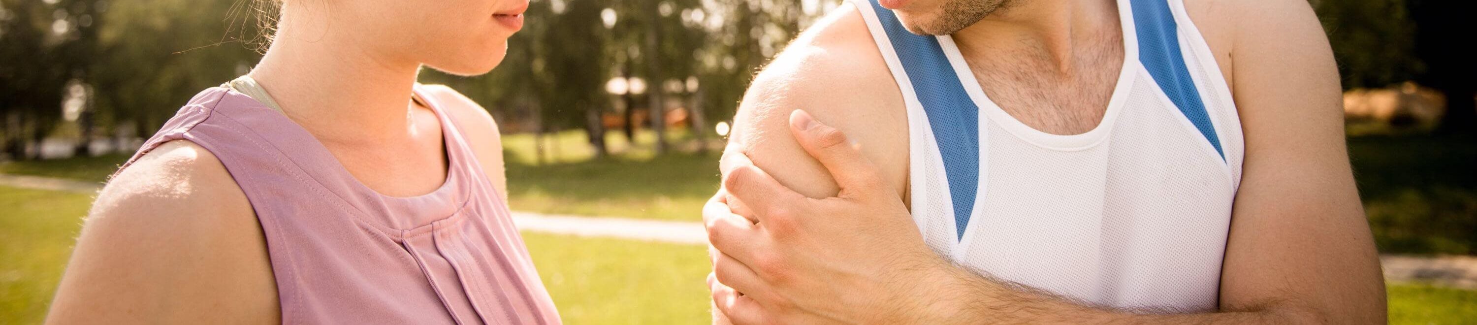 Person holding an upper arm outdoors, illustrating shoulder pain or discomfort during physical activity.