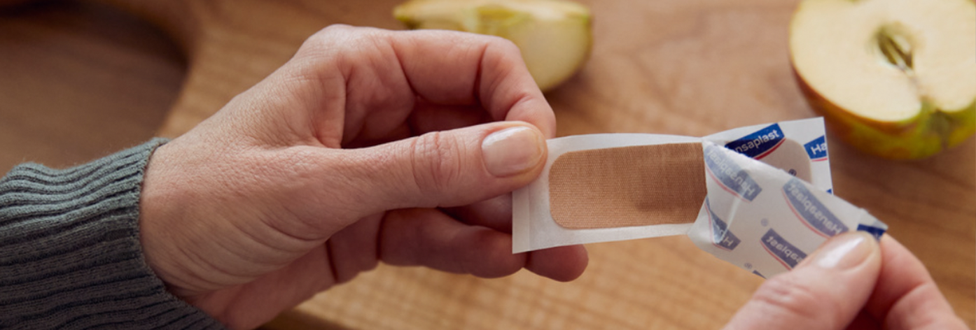 Une personne ouvre un pansement Hansaplast.