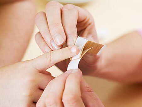 Nahaufnahme der Hände einer erwachsenen Frau, die ein Pflaster auf den verletzten Finger eines Kindes aufklebt.
