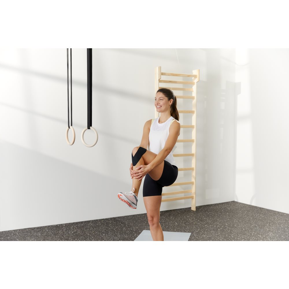 Frau im Fitnessraum mach Übung mit Kniesiologie Tapes an Armen und Beinen