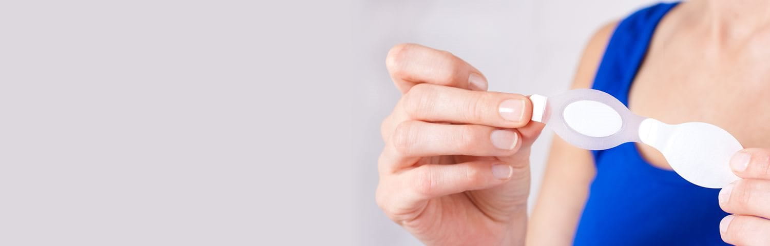 Frau die ein transparentes Pflaster zwischen den Fingern hält.