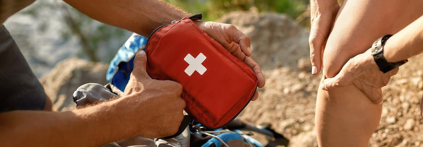 Mann holt Reiseapotheke aus Rucksack für verletztes Knie der Frau