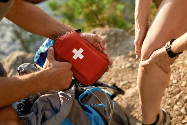 Mann holt Reiseapotheke aus Rucksack für verletztes Knie der Frau