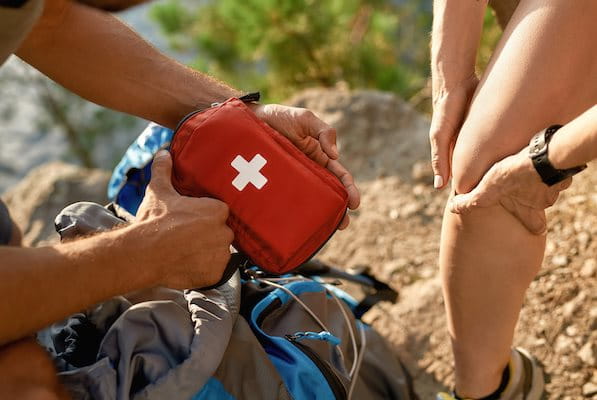Mann holt Reiseapotheke aus Rucksack für verletztes Knie der Frau