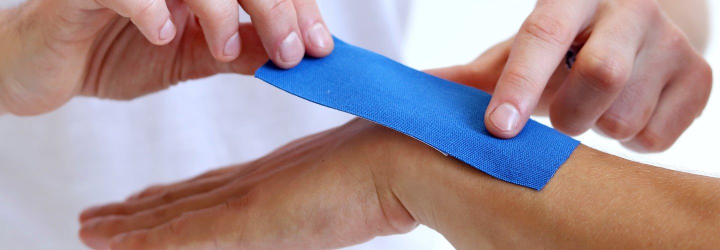 Aufkleben von Kinesiologie Tape auf einem Handgelenk