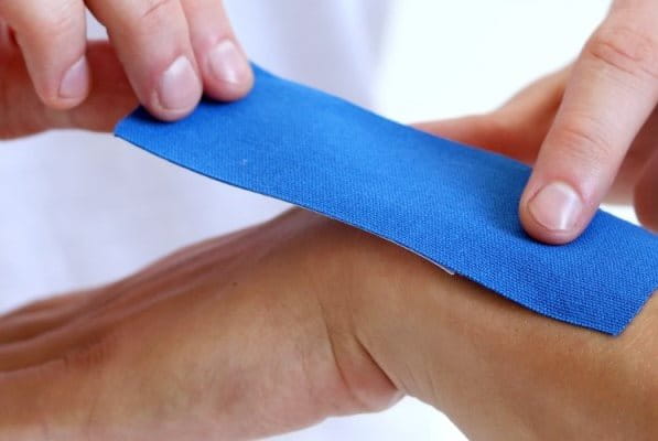 Aufkleben von Kinesiologie Tape auf einem Handgelenk