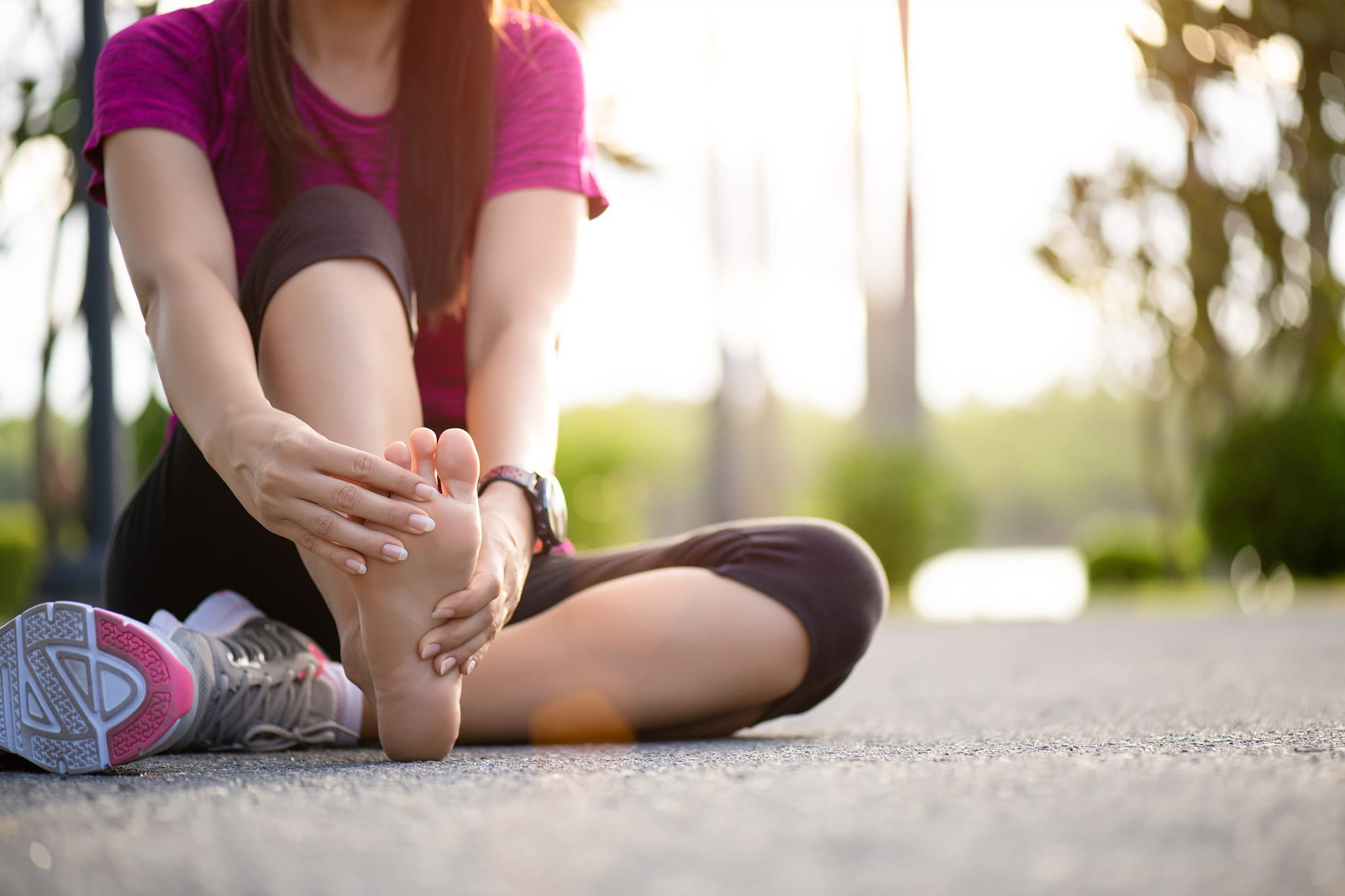 Sportlerin sitzt auf dem Boden und hält sich den verletzten Fuß.