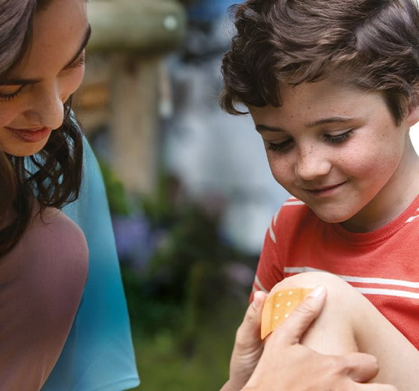 A woman placing plaster to a kid.