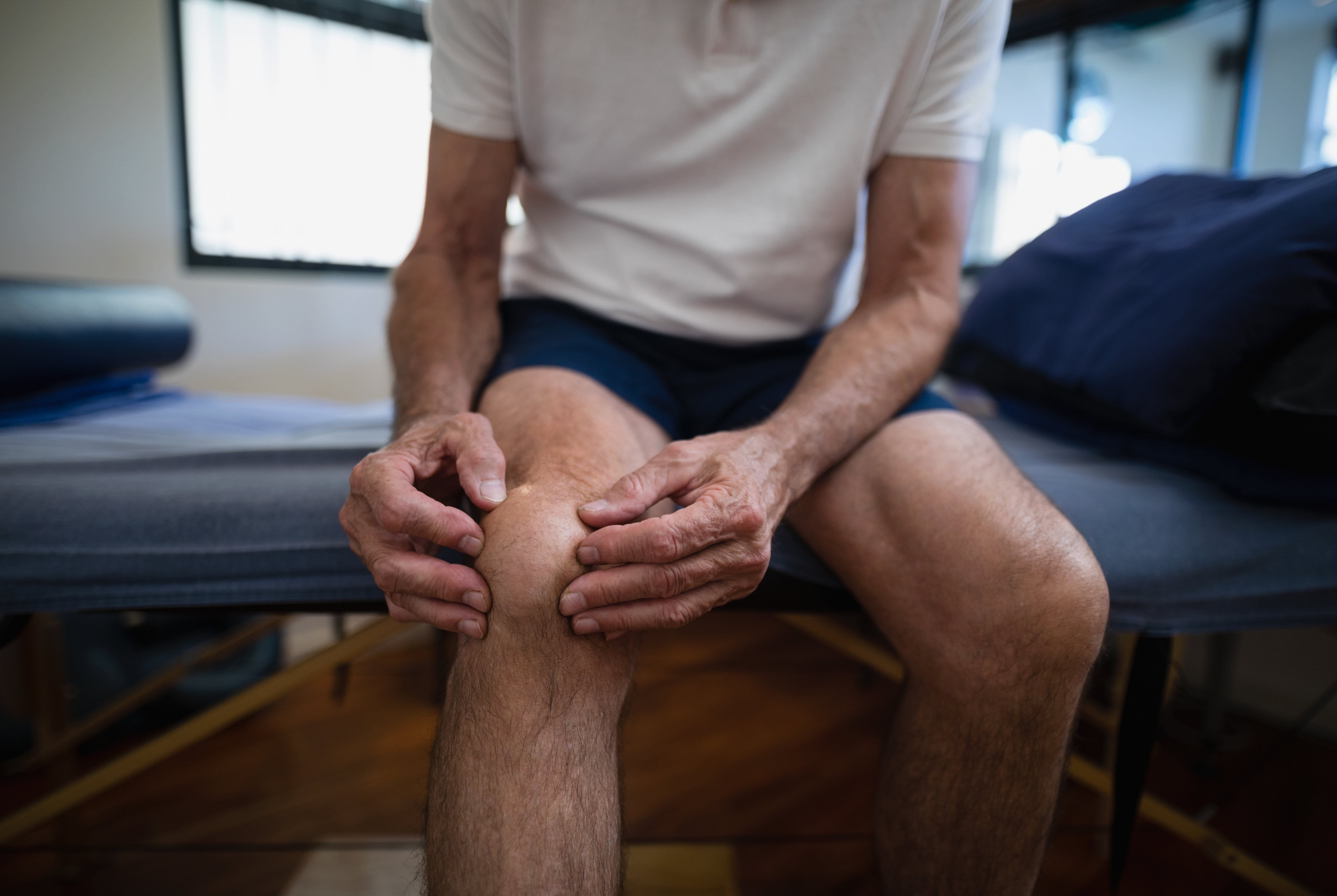 Male patient sitting holding knee in pain