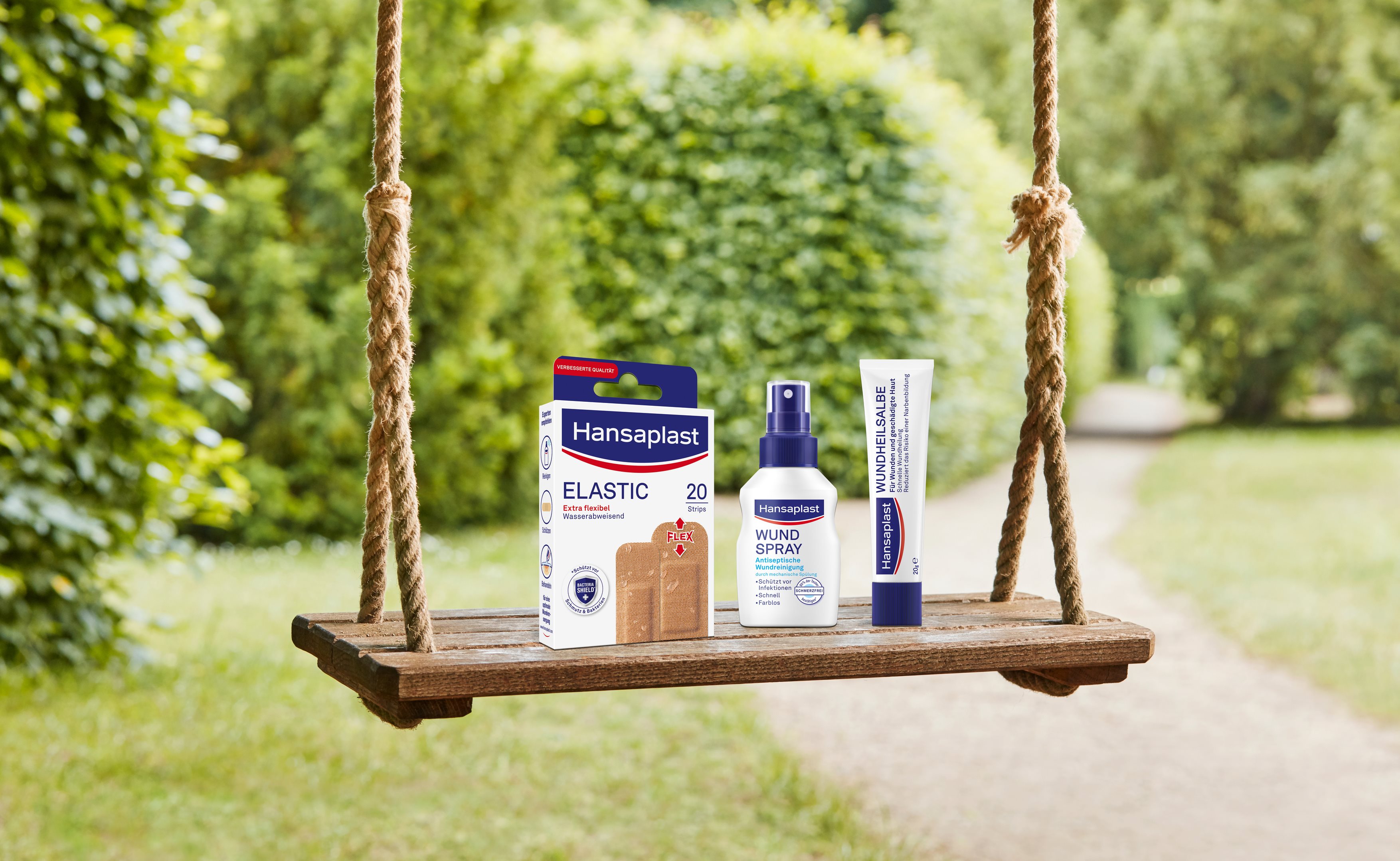 Hansaplast Elastic-Pflaster, Wundspray und Wundheilsalbe, präsentiert auf einer Holzschaukel im Freien.