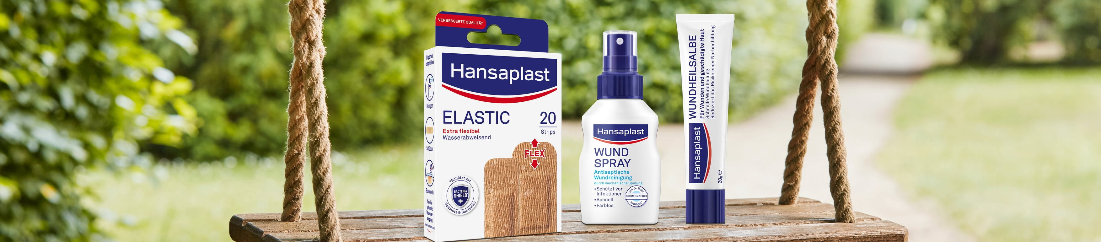 Hansaplast Elastic-Pflaster, Wundspray und Wundheilsalbe, präsentiert auf einer Holzschaukel im Freien.