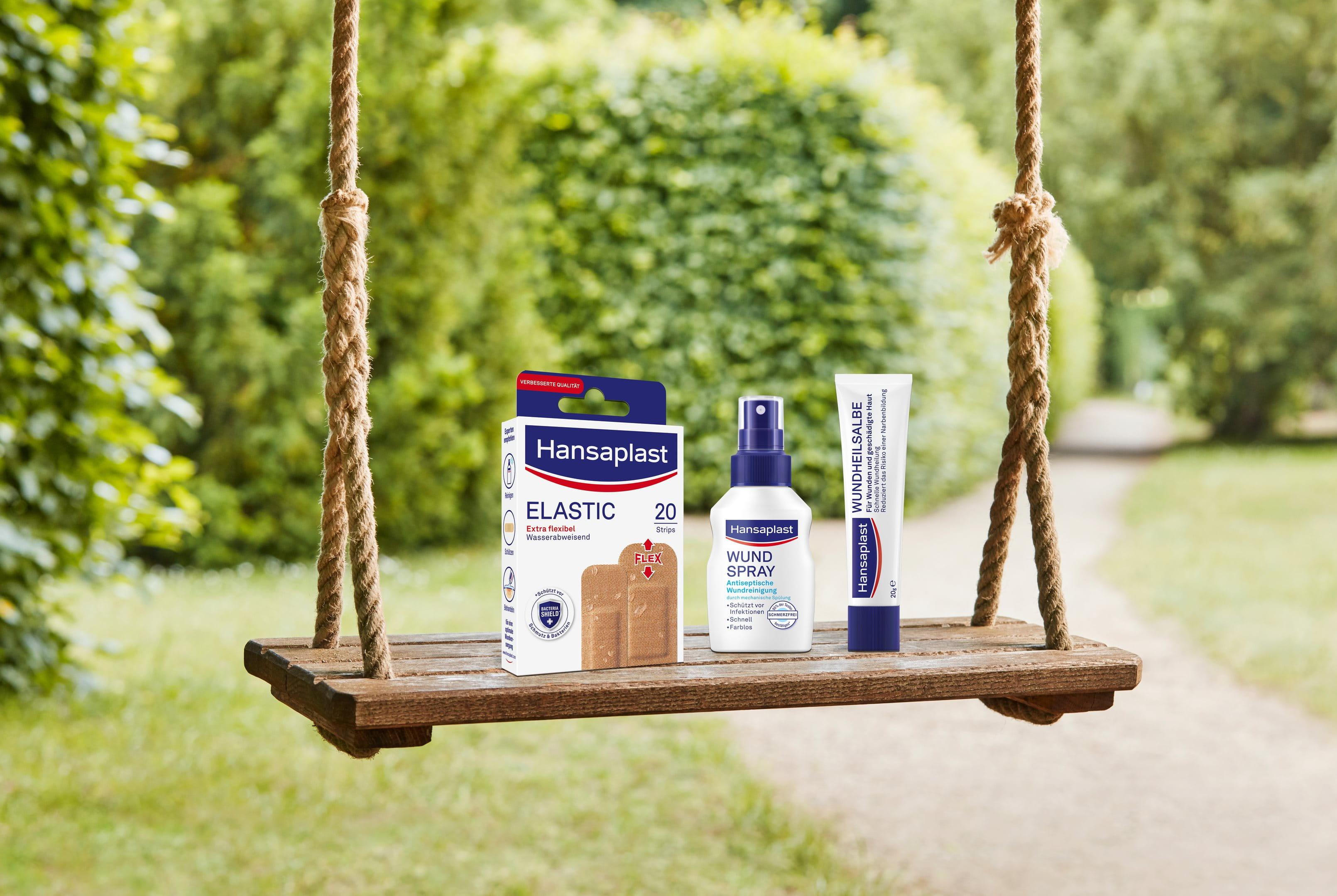Hansaplast Elastic-Pflaster, Wundspray und Wundheilsalbe, präsentiert auf einer Holzschaukel im Freien.