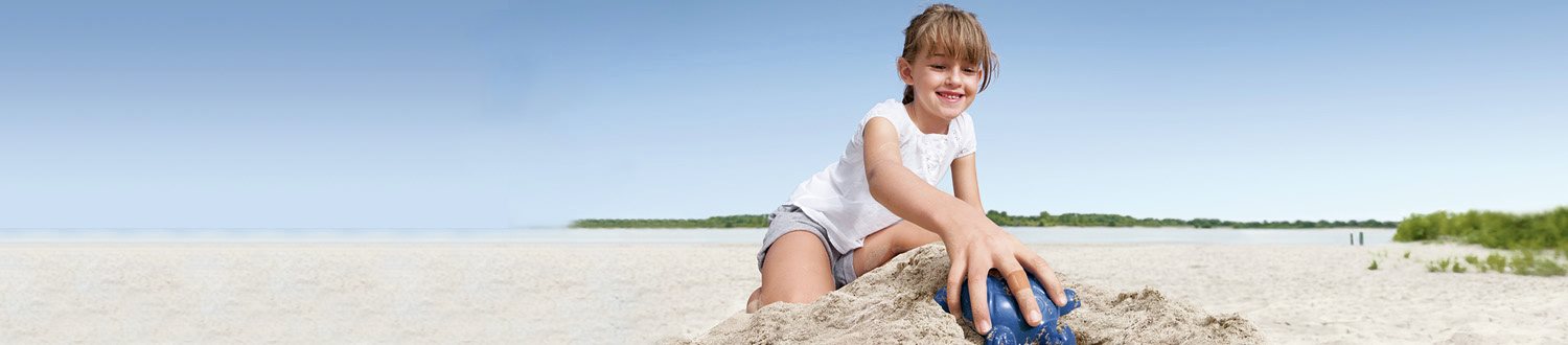 A young girl on a yellow tricycle smiles as she skids across a gravel path
