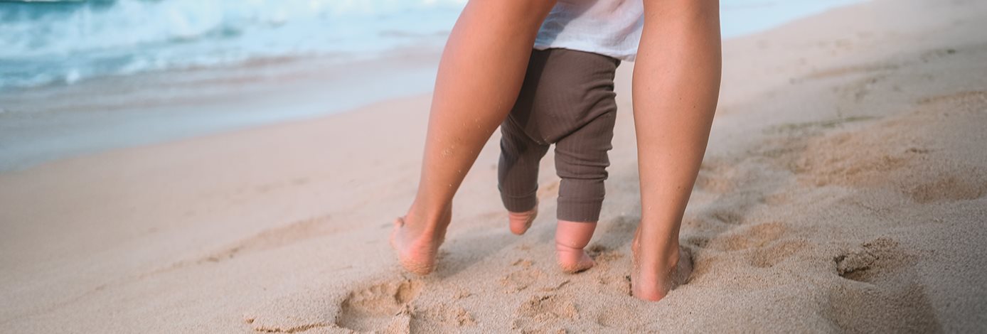 Die Beine eines Erwachsenen und eines Kindes am Strand