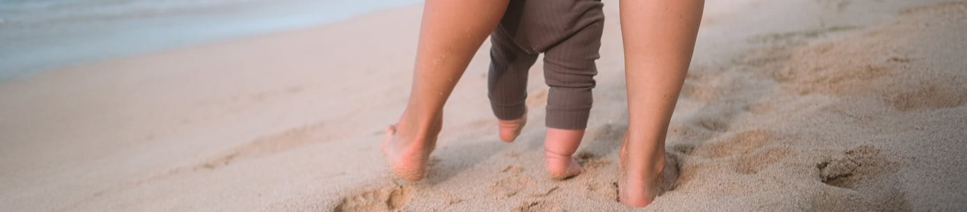 Die Beine eines Erwachsenen und eines Kindes am Strand