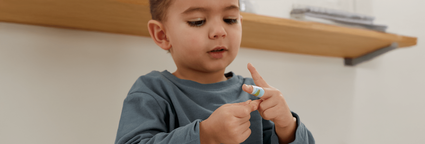 Ein Kind schaut auf seinen Finger, an dem ein buntes Pflaster klebt.