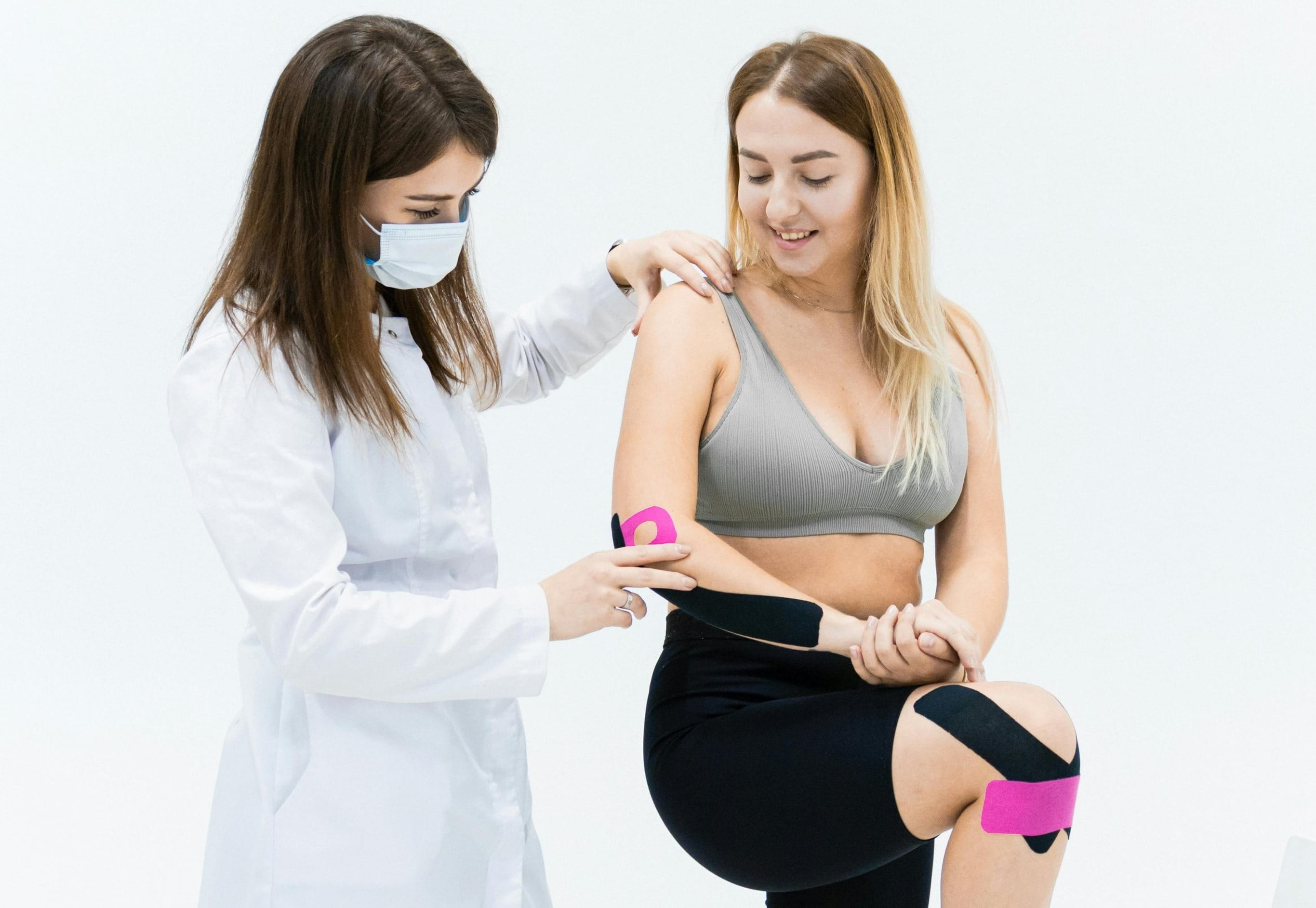 Eine Ärztin klebt einer Frau Kinesio Tape auf den Körper auf.