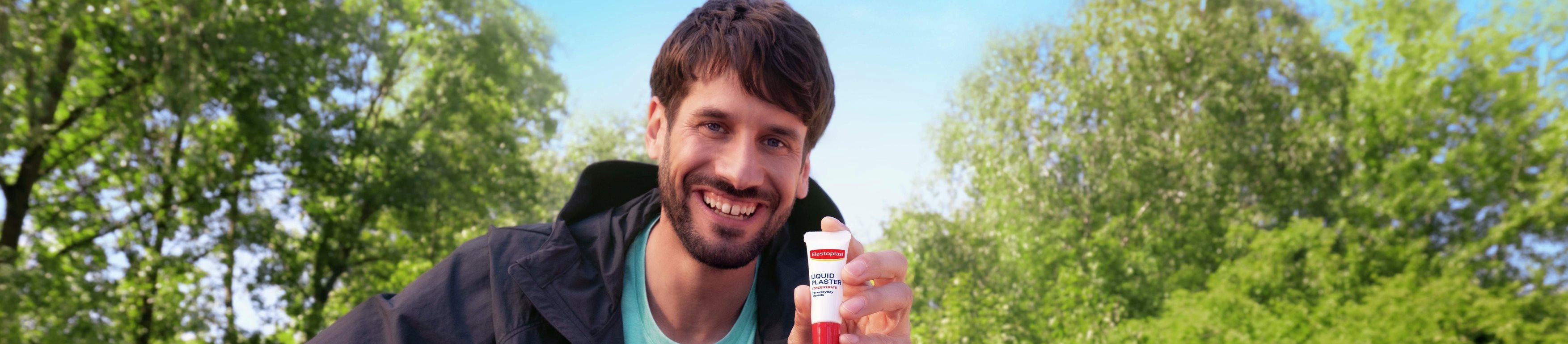 Un homme souriant, assis sur un banc de parc en plein air.