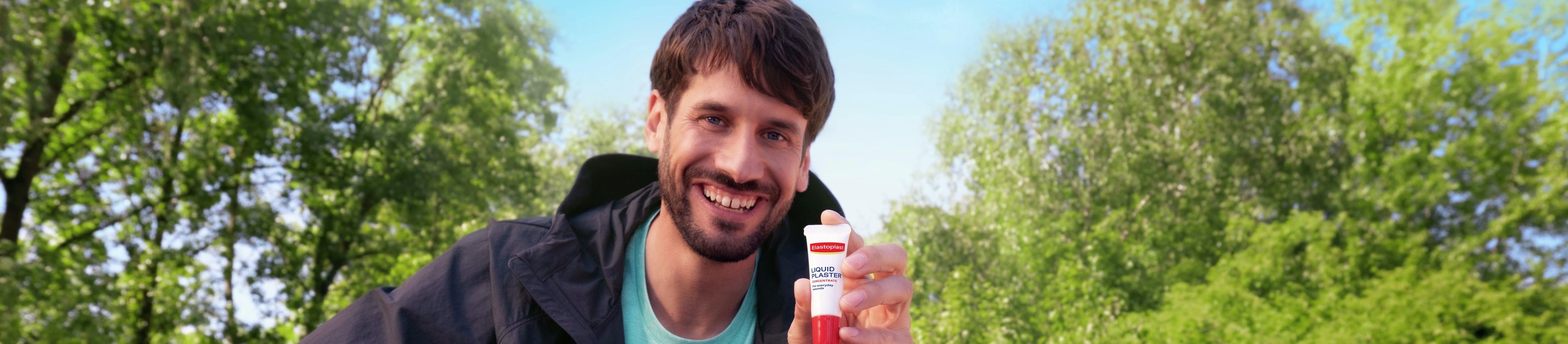 Un homme souriant, assis sur un banc de parc en plein air.